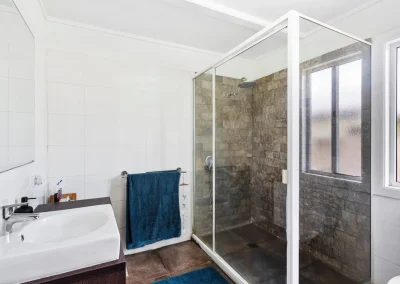 Bathroom with worn stone shower tiles and framed screen before bathroom renovation at Main Beach