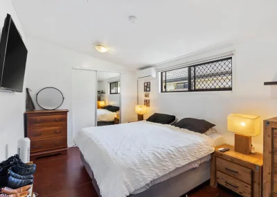 Bedroom with dark timber floors, bedside tables and louvre windows before home renovation at Main Beach